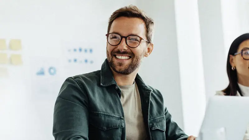 Photograph of a smiling person wearing glasses in a white room