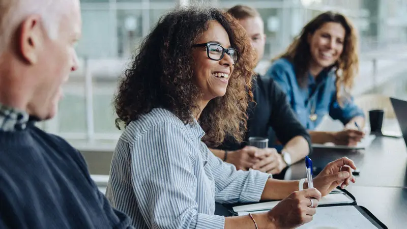 Photograph of a smiling person in a business meeting with several other people