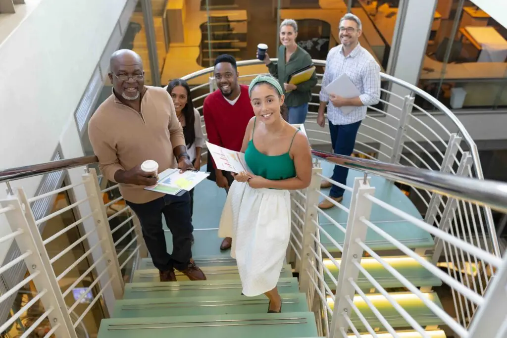 High angle portrait of happy biracial male and female advisors standing at staircase in workplace. unaltered, business, teamwork and modern office concept.