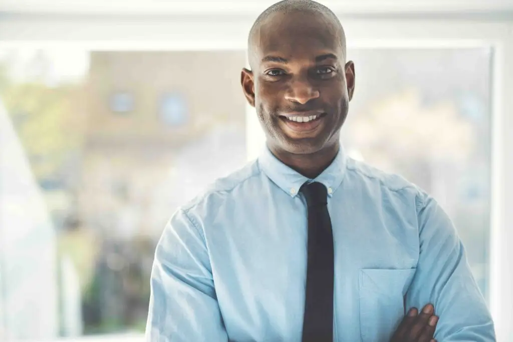 Smiling African businessman wearing a shirt and tie standing with his arms crossed in his home office